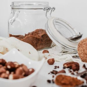 Glass jar with cocoa powder amidst ingredients in a rustic setting. Perfect for food enthusiasts and recipes.