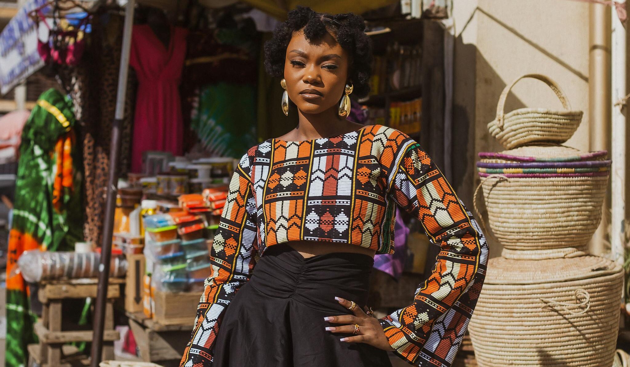 Stylish woman poses in vibrant traditional attire at an outdoor market.
